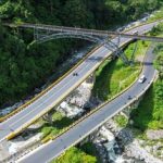Jembatan di atas lembah sungai dengan jalan beraspal yang melintas di kawasan hijau