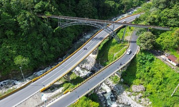 Jembatan di atas lembah sungai dengan jalan beraspal yang melintas di kawasan hijau