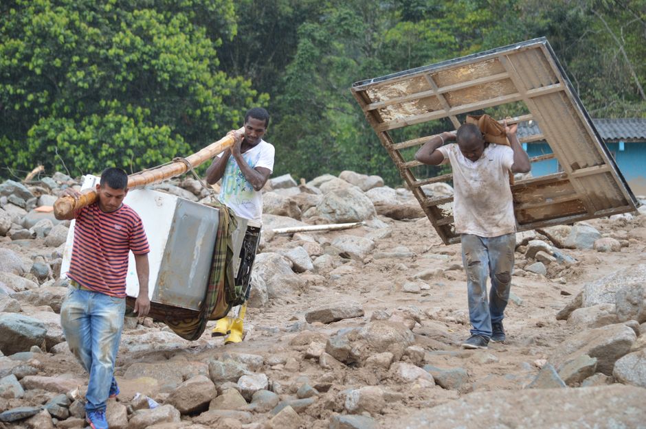 Sejumlah pria menyelamatkan barang-barang di tengah reruntuhan bangunan akibat longsor