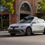 Mobil robotaksi Waymo berwarna putih melaju di jalan kota dengan perangkat sensor di atapnya