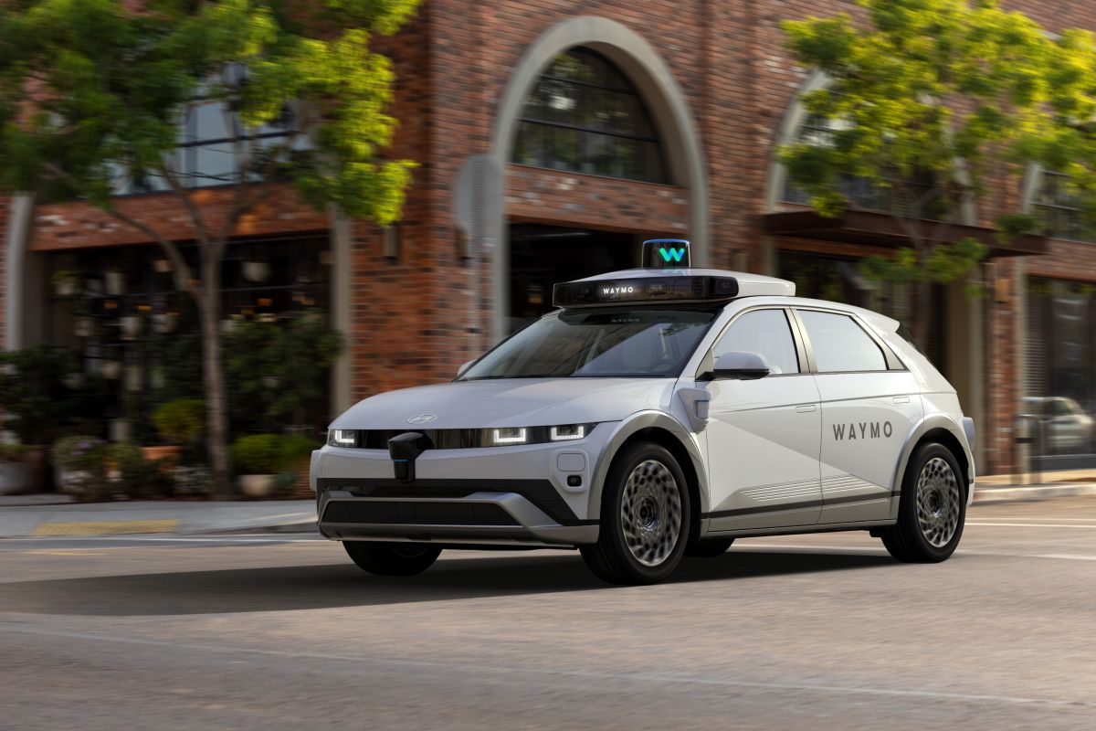 Mobil robotaksi Waymo berwarna putih melaju di jalan kota dengan perangkat sensor di atapnya