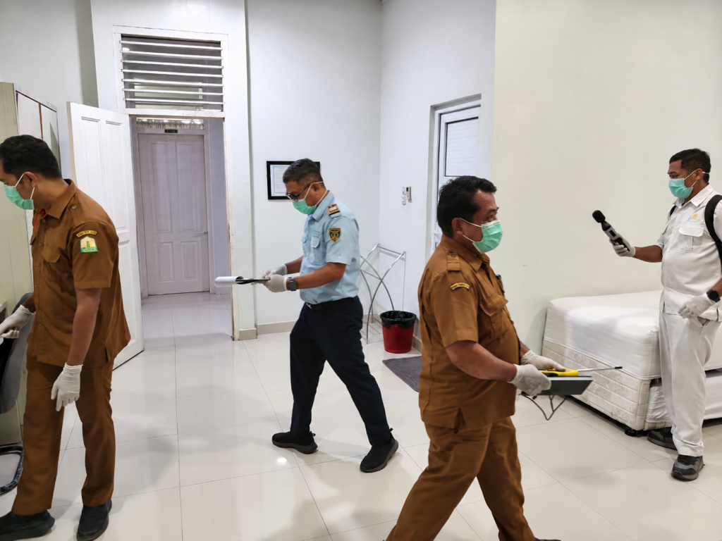 Petugas berseragam memakai masker dan sarung tangan memeriksa kamar asrama haji