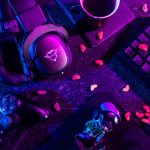 Headset, kontroler, dan keyboard gim di atas meja dengan pencahayaan ungu