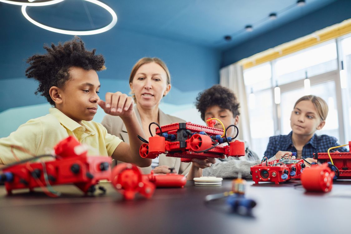 Guru dan siswa mengerjakan proyek robotik dengan model robot merah di ruang kelas