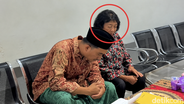 Seorang perempuan dan laki-laki berpeci duduk berdampingan di ruang tunggu Polres Pamekasan selama proses pemeriksaan