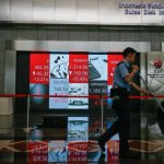 Papan indeks Bursa Efek Indonesia menampilkan angka-angka merah yang menurun dan seorang pekerja membersihkan lantai