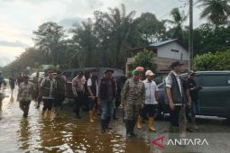 Rombongan pejabat berjalan menyusuri jalan permukiman yang tergenang banjir