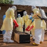 Petugas kesehatan berbusana pelindung kuning menangani jenazah di depan sebuah bangunan di wilayah wabah Ebola