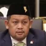 Seorang legislator berpeci hitam dan jas duduk di kursi rapat