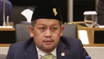 Seorang legislator berpeci hitam dan jas duduk di kursi rapat