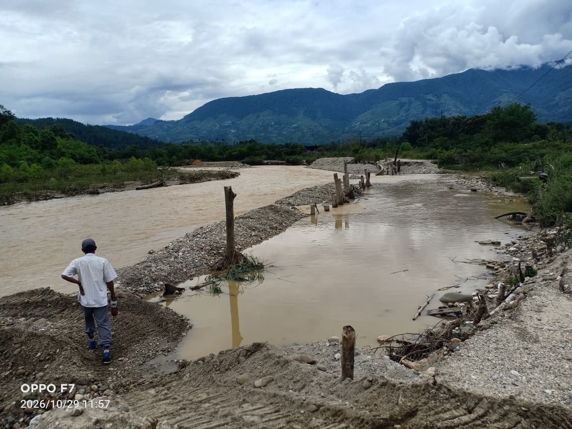 Seorang warga berdiri di tepi tanggul sungai yang belum selesai ditimbun di Aih Bobo, Gayo Lues, dengan genangan air keruh dan pegunungan di latar