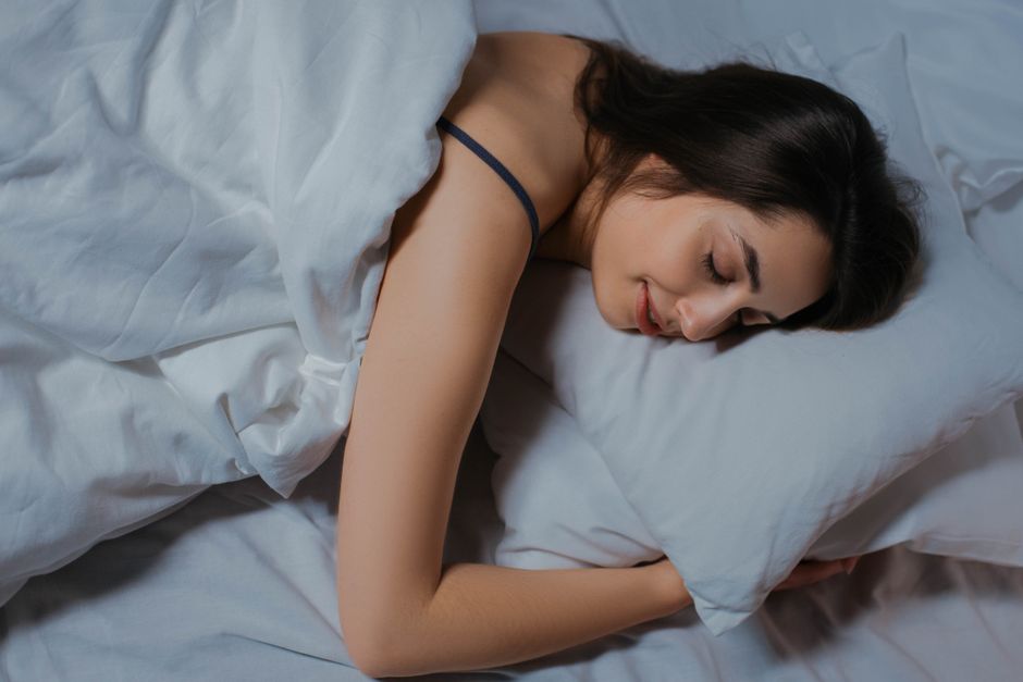 Seorang perempuan tidur nyenyak di atas tempat tidur dengan selimut putih