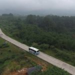 Bus melaju di jalan pedesaan yang membelah perbukitan hijau