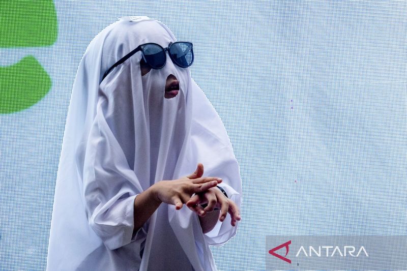Seorang anak berkostum hantu putih memakai kacamata hitam dalam lomba busana Halloween