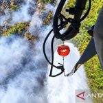 Helikopter menjatuhkan air dari wadah gantung ke lahan terbakar yang berasap