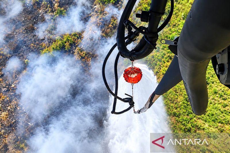 Helikopter menjatuhkan air dari wadah gantung ke lahan terbakar yang berasap