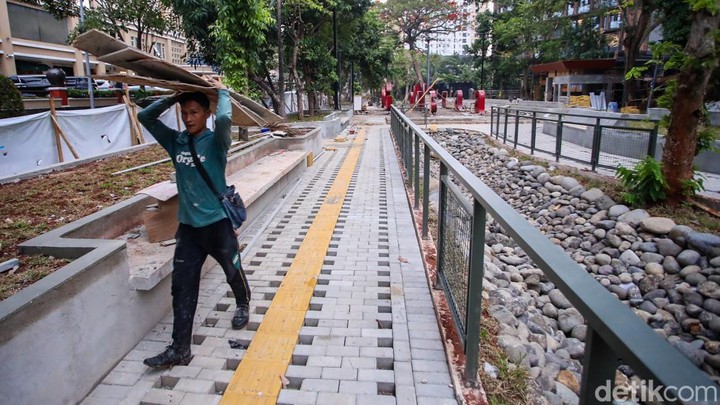 Seorang pekerja membawa papan di jalur taman yang sedang direvitalisasi di Jakarta