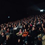 Penonton di bioskop saat festival film, suasana gelap dengan layar menyala