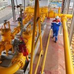 Instalasi pipa gas berwarna kuning dengan pekerja berseragam biru dan helm putih