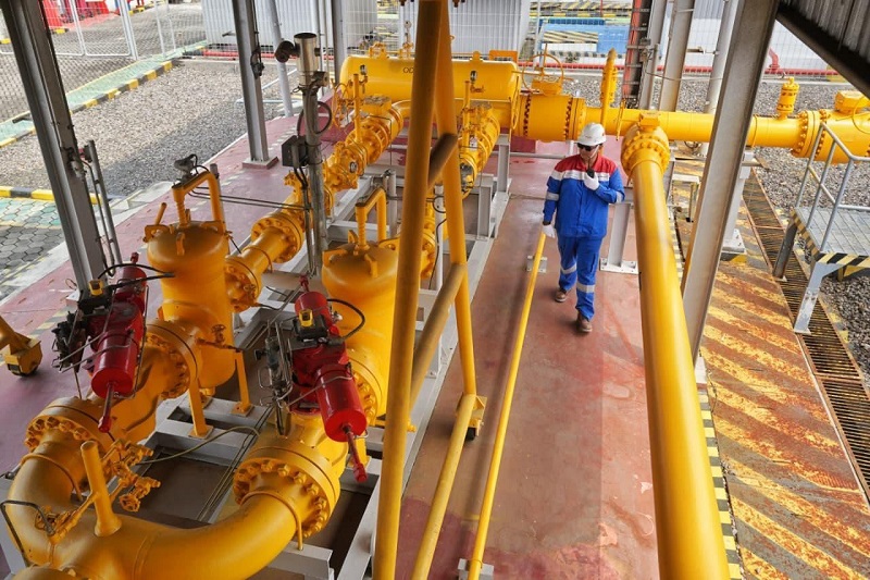 Instalasi pipa gas berwarna kuning dengan pekerja berseragam biru dan helm putih