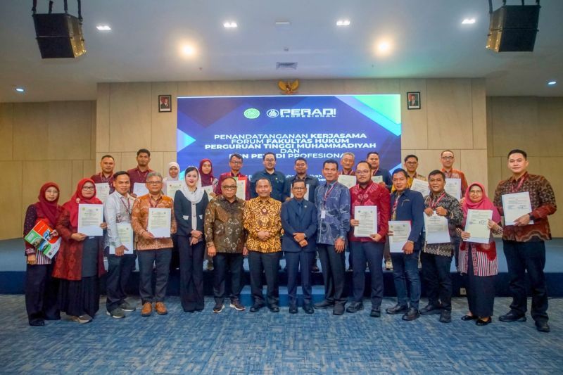 Sekelompok orang berfoto bersama memegang sertifikat di depan spanduk penandatanganan kerja sama PERADI dan perguruan tinggi Muhammadiyah.