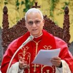 Paus Leo XIV berjubah merah sedang membaca dokumen sambil duduk di kursi kayu berukir
