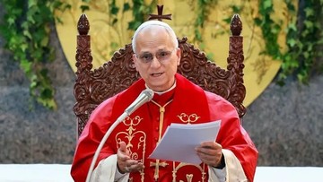 Paus Leo XIV berjubah merah sedang membaca dokumen sambil duduk di kursi kayu berukir