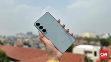 Tangan memegang ponsel Samsung Galaxy berwarna terang dengan tiga kamera belakang di atas latar kota