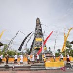 Umat Hindu berpakaian adat berjalan mengelilingi candi dalam ritual di halaman pura dengan umbul-umbul warna-warni