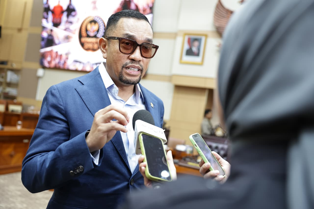 Ahmad Sahroni berbicara kepada wartawan yang memegang mikrofon dan ponsel.