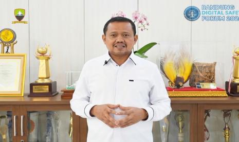 Seorang pejabat berbicara di depan kamera dengan latar deretan piala dan logo Bandung Digital Safety Forum 2026