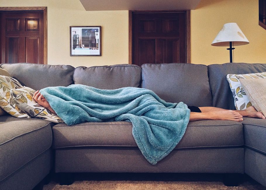 Seseorang tidur siang berselimut biru di atas sofa ruang tamu