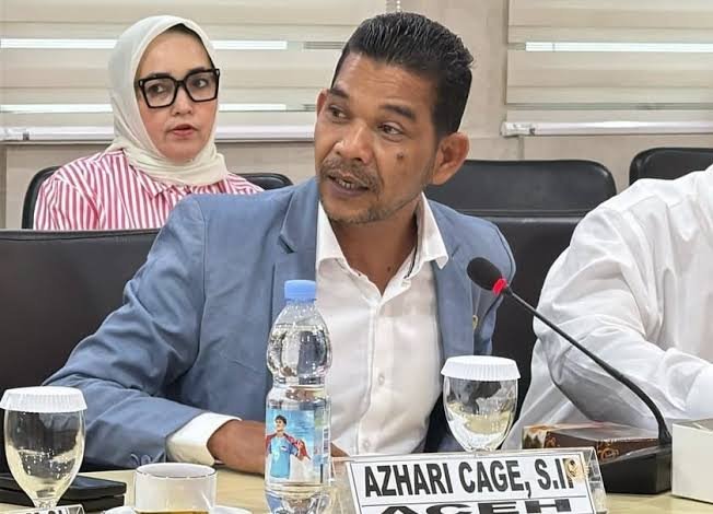 Azhari Cage berbicara dalam sebuah rapat, dengan papan nama di depannya