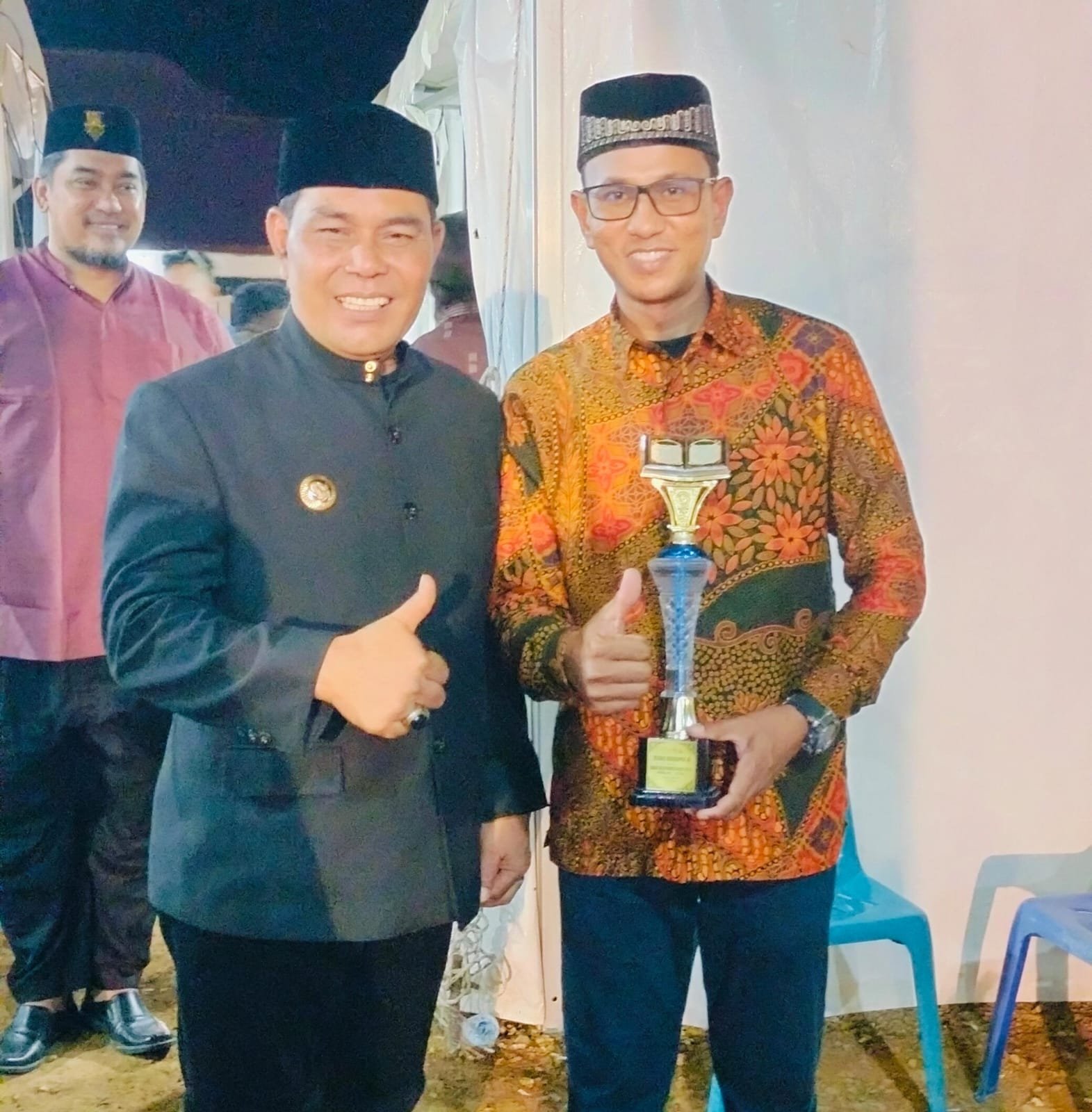 Seorang pria berbaju batik memegang piala sambil mengacungkan jempol pada malam penganugerahan MTQ