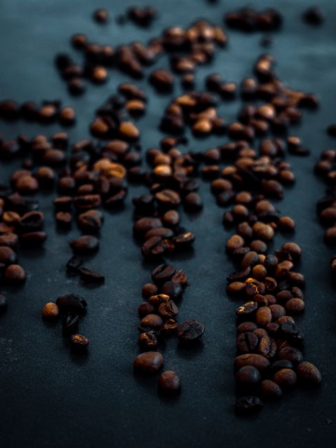 Biji kopi sangrai dari dekat yang tersebar di atas permukaan gelap, menampakkan tekstur dan warnanya