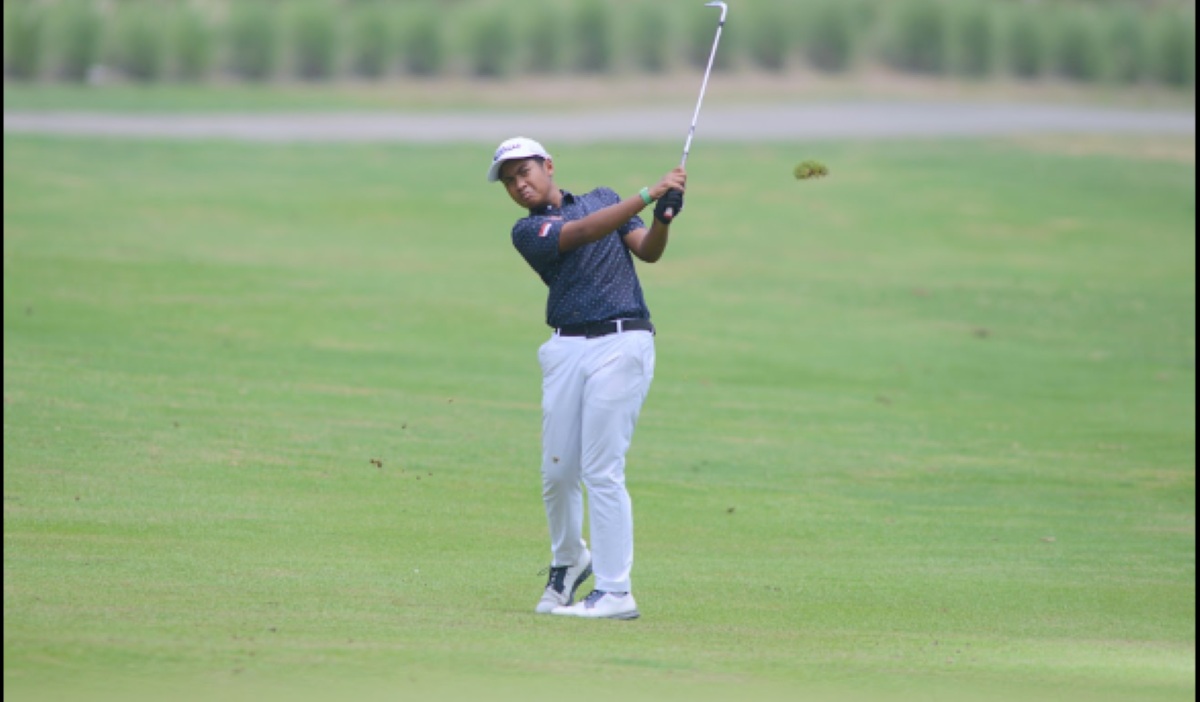 Pegolf muda melakukan ayunan stik golf di lapangan hijau
