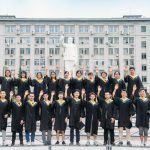 Para lulusan berbusana toga berpose di depan gedung universitas