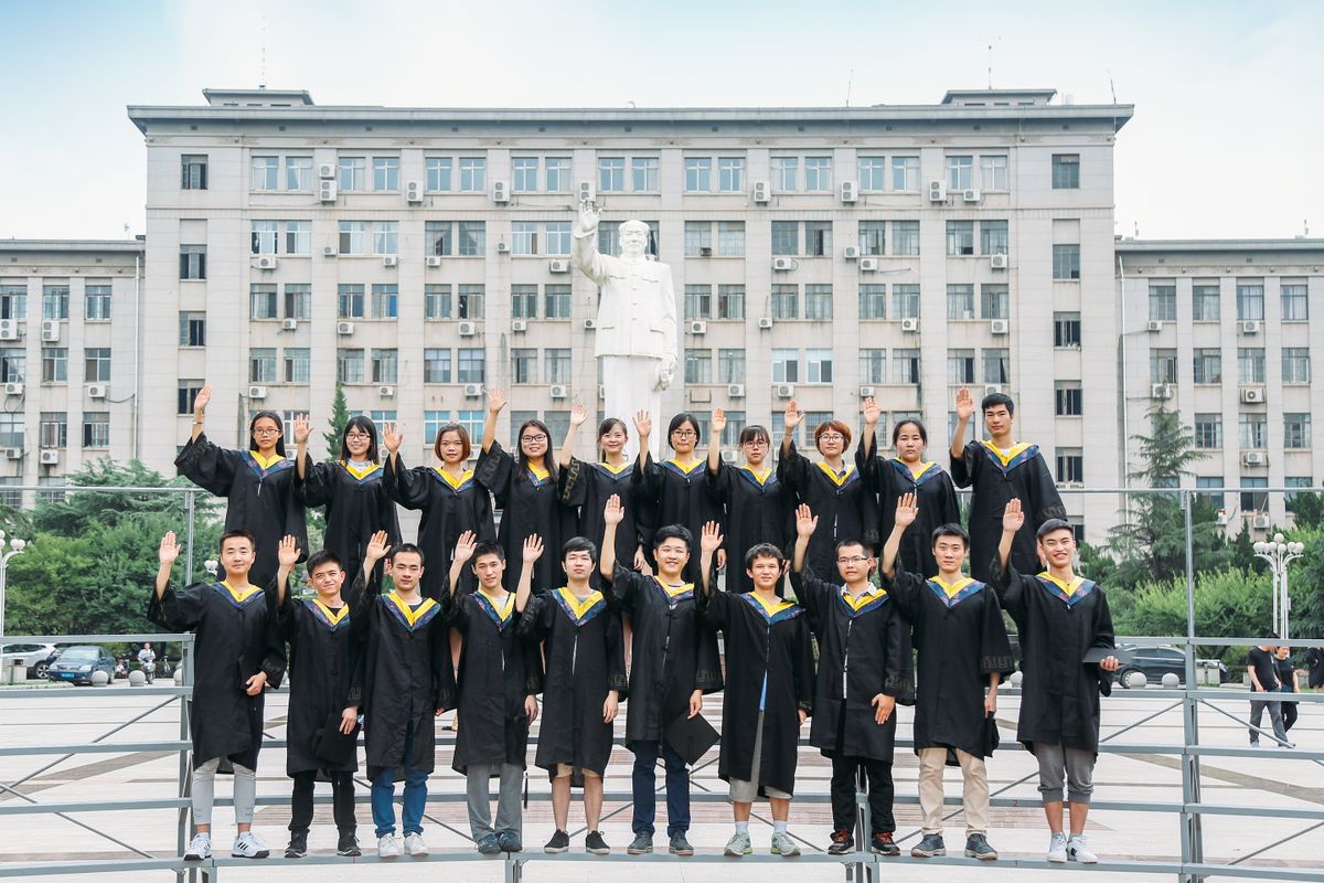 Para lulusan berbusana toga berpose di depan gedung universitas