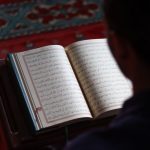 Seseorang membaca Al-Qur'an di dalam masjid dengan karpet bermotif