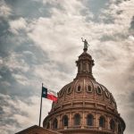 Kubah Gedung Capitol Negara Bagian Texas di Austin dengan bendera Texas berkibar di sampingnya di bawah langit berawan
