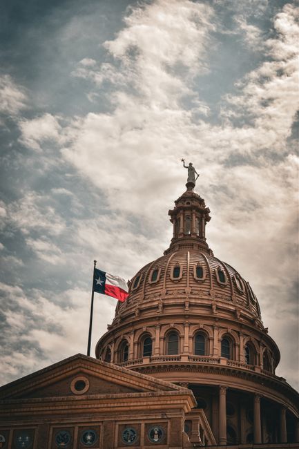 Kubah Gedung Capitol Negara Bagian Texas di Austin dengan bendera Texas berkibar di sampingnya di bawah langit berawan