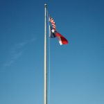 Bendera Texas dan bendera Amerika Serikat berkibar pada tiang tinggi di bawah langit biru cerah